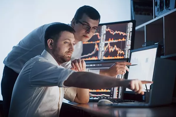 team-of-stockbrokers-are-having-a-conversation-in-a-dark-office-with-display-screens-analyzing-data-graphs-and-reports-min